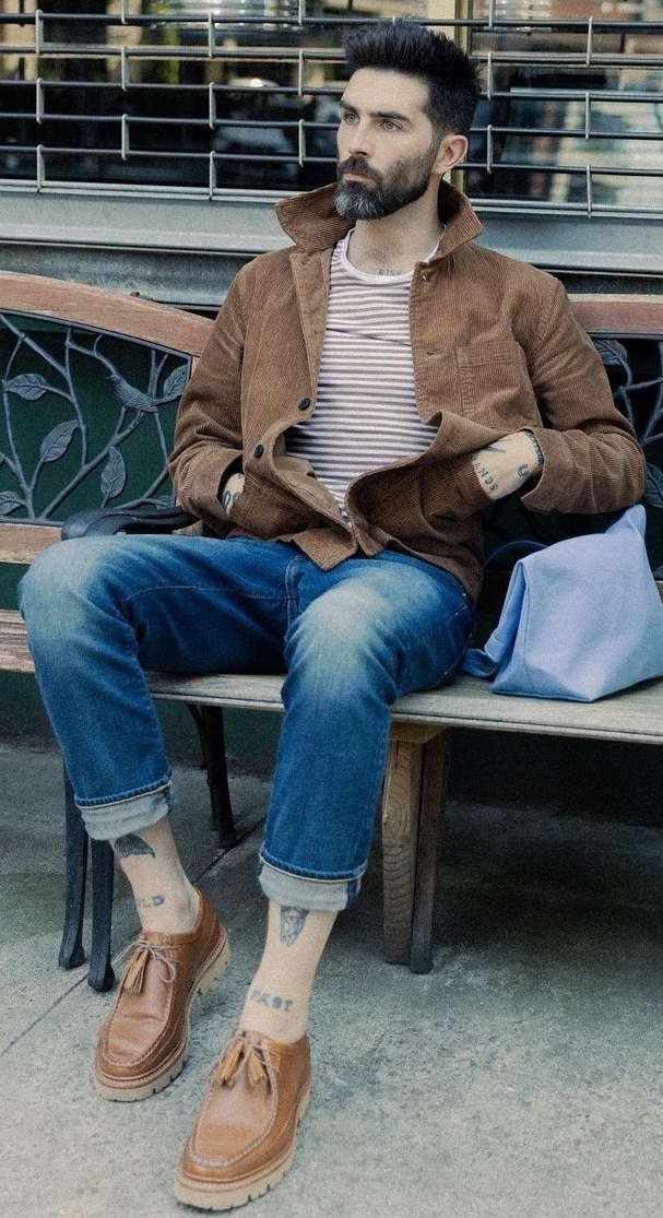 beige and white stripped t-shirt with brown jacket and blue denims with blue side bag