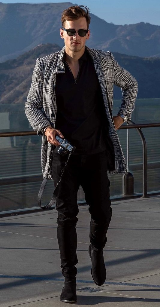 black formal shirt with black chinos and checkered overcoat accessorized with shades and a camera in hand