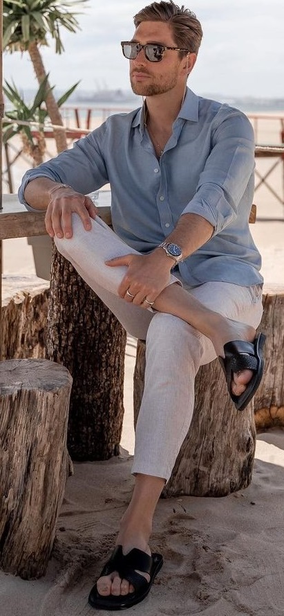 blue shirt with white chinos and black slippers accessorized with shades and a watch