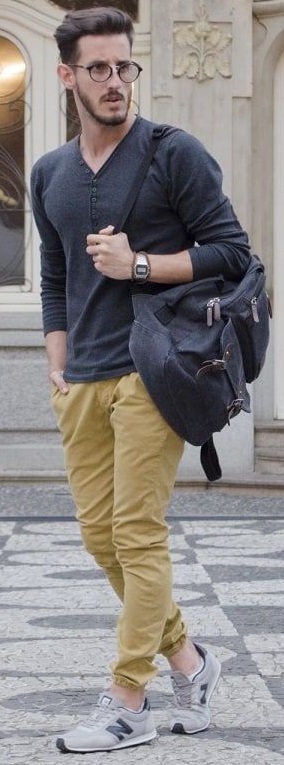 beige chino joggers with grey full-sleeved tshirt and shades, accessorized with glasses and watch holding a bag in shoulders