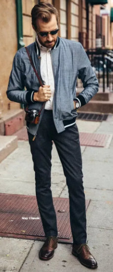 Brogue leather shoes with bla chinos and a white shirt with a blue color zipper jacket accessorized with shades, a watch and a camera in hand
