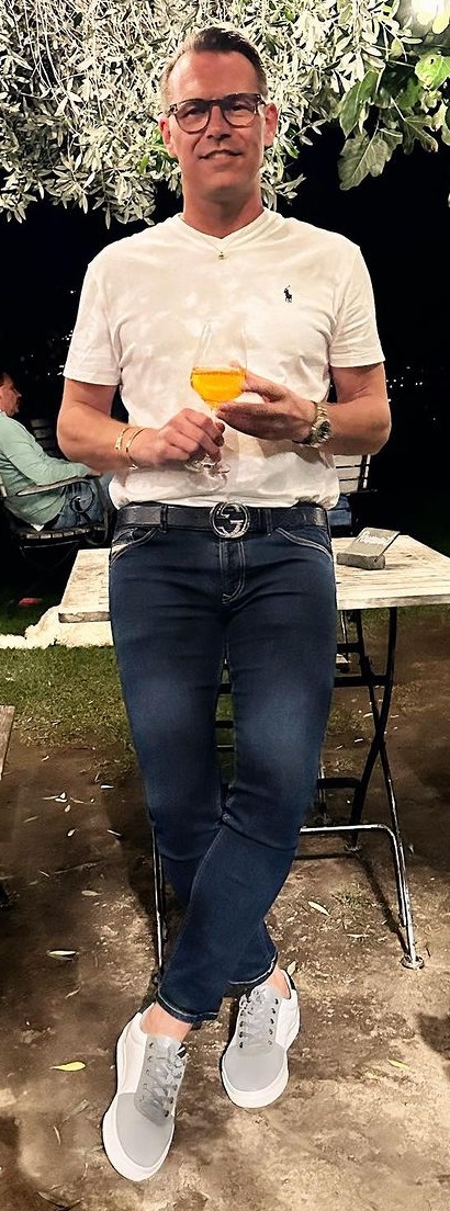 a blue denim with a white tshirt, accessorized with a Gucci belt being a must-have product to own with glasses and a watch and a glass of drink